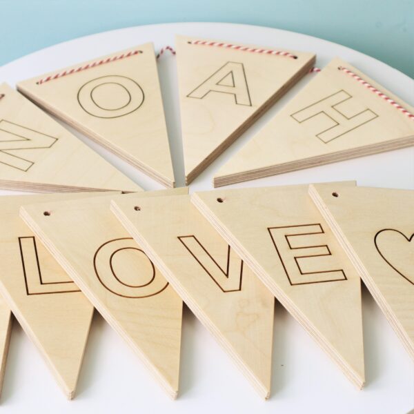 Wooden ply bunting triangles laid out on a table with the words LOVE and NOAH spelled out.