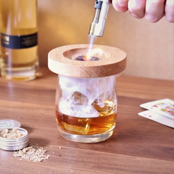 Solid oak whiskey smoker placed on a glass with a blow torch burning sawdust to create smoke